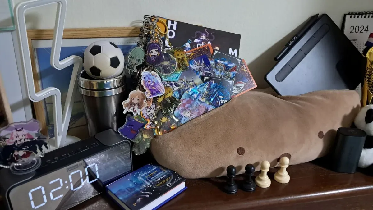 Shelf on my desk with acrylic charms, a drawing tablet, a soft toy, chess pieces and a football.