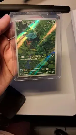 A hand holding a Japanese holo Pokemon card in a hard plastic case.